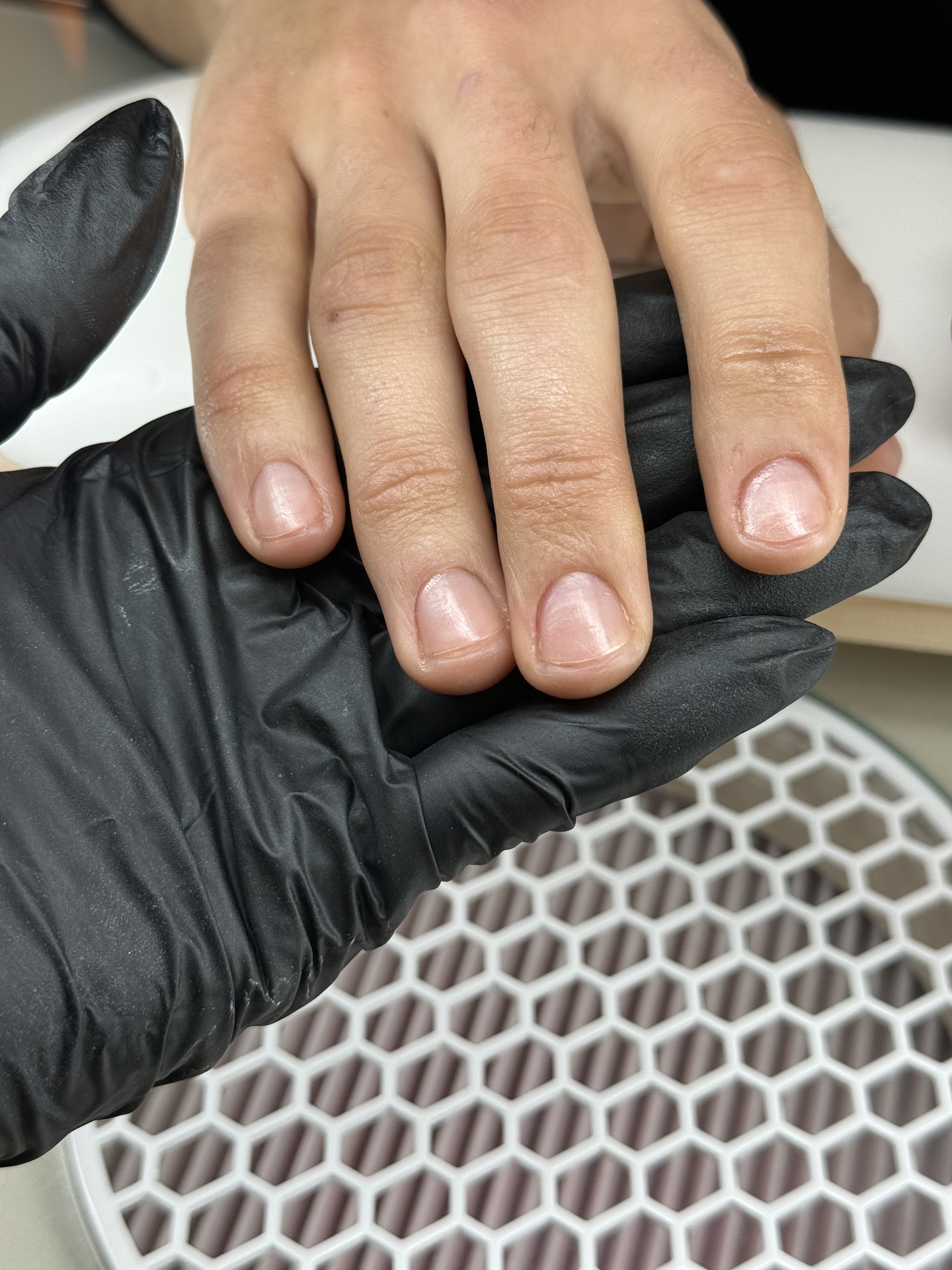 Korte nude nagels op een zwarte handschoen boven een witte lamp