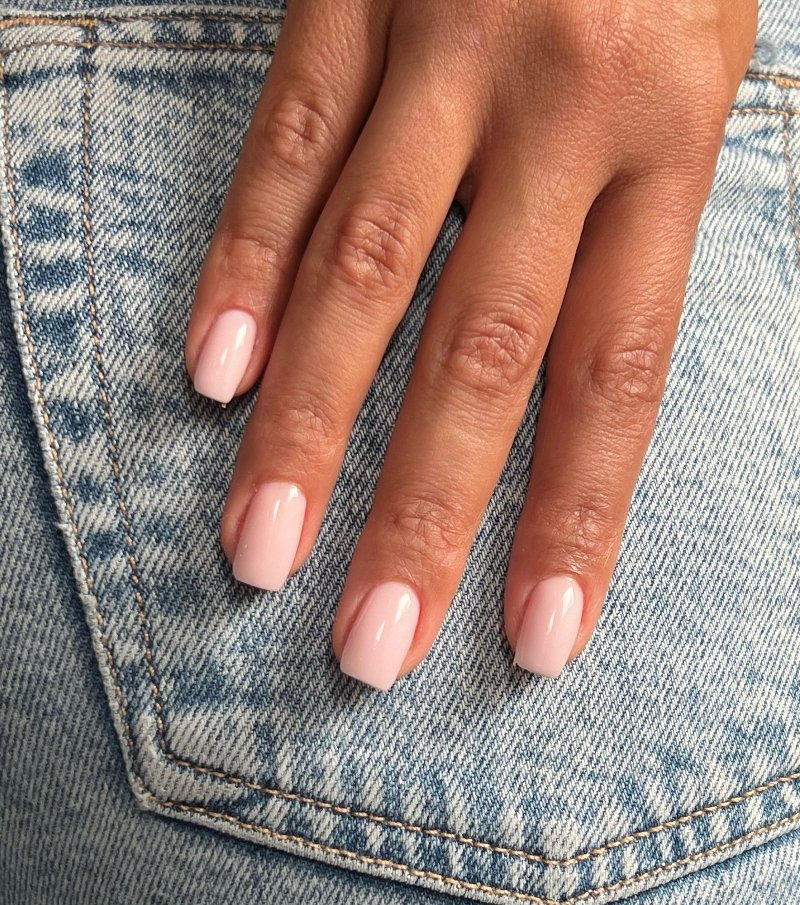 Korte nude nagels tegen een spijkerbroek